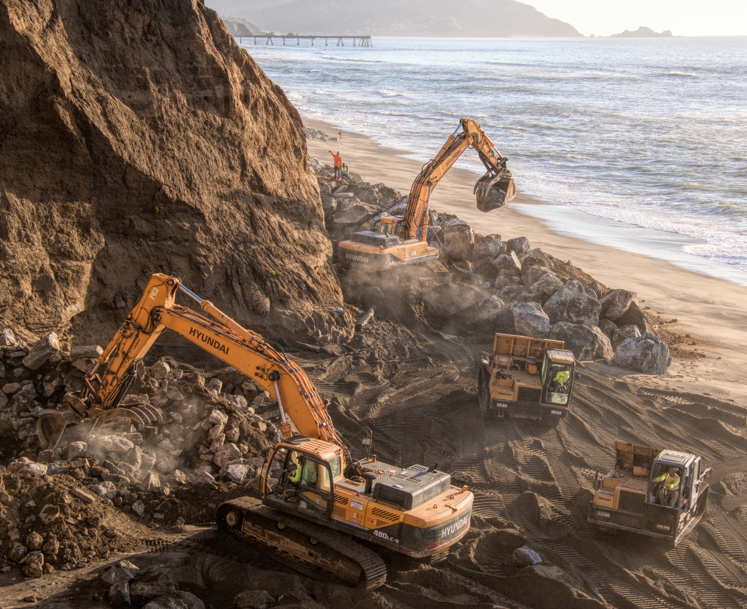 Workers positioning large boulders at the base of a Pacifica cliff in an attempt to prevent further erosion.