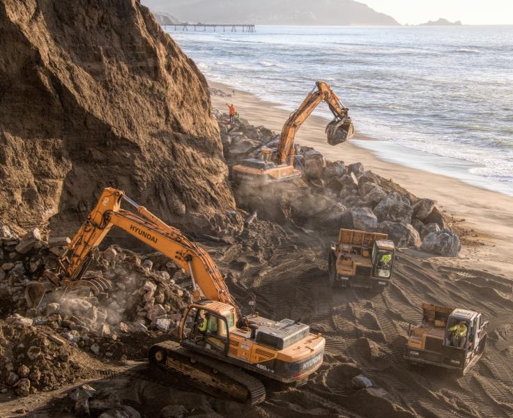 Workers positioning large boulders at the base of a Pacifica cliff in an attempt to prevent further erosion.