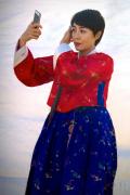 Korean woman in traditional costume checks her appearance with her smart phone.